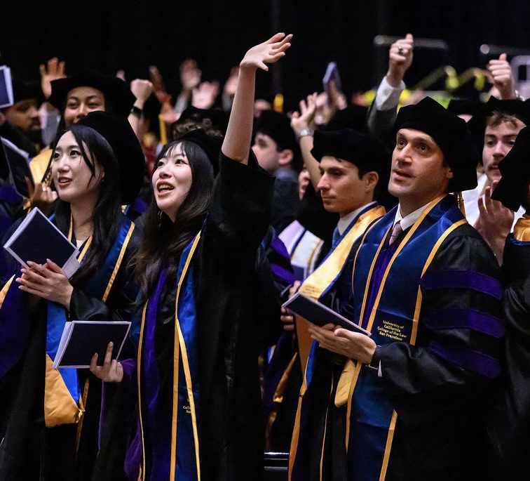 A crowd of graduates smiling and celebrating, one with her arm extended in the air in celebration.
