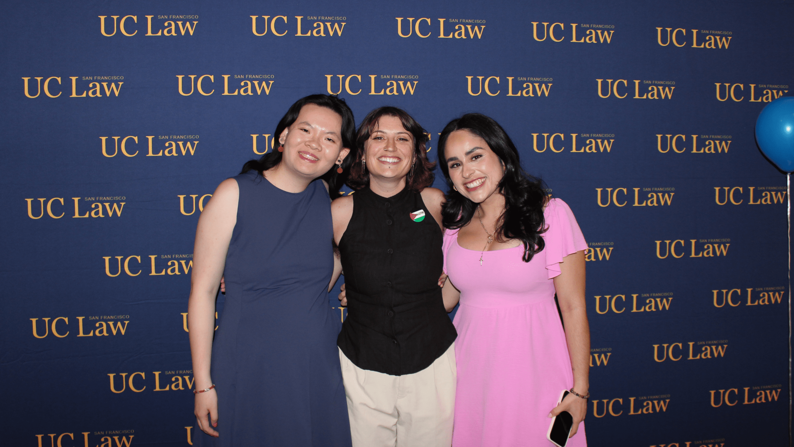 Three students smiling while standing in front of a UC Law SF backdrop