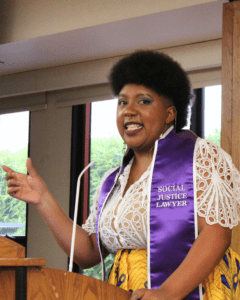 Graduate Amirah Tulloch speaking in the Alumni Reception Center. She is wearing the purple Social Justice Concentration stole that says "social justice lawyer"