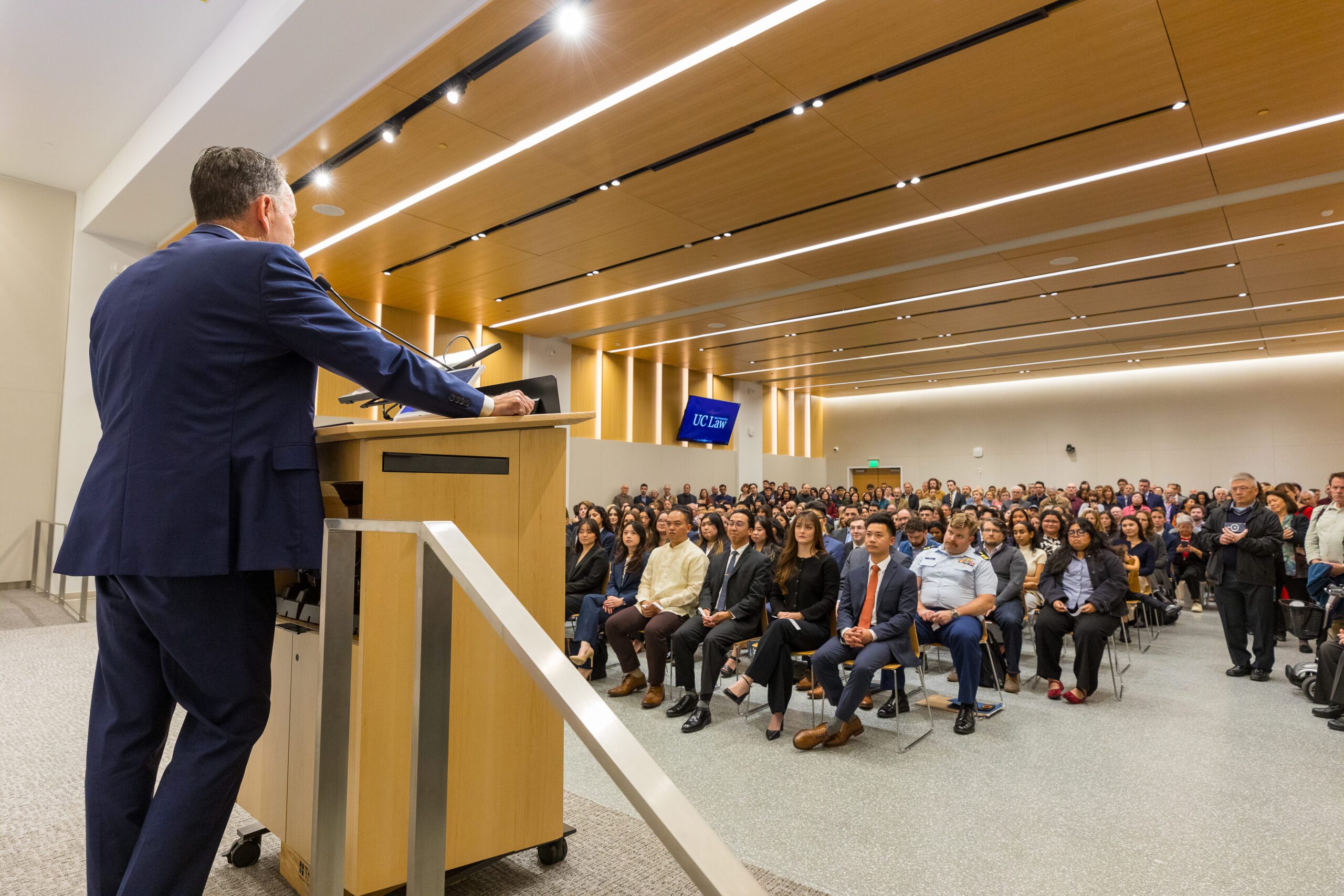 A speaker behind a podium looks out into a large audience of people in 198 McAllister's auditorium