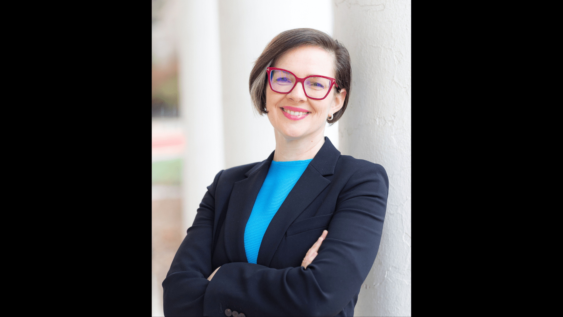 A headshot of Moira O'Neill donning red glasses, a light-blue shirt, and a navy-blue blazer.