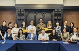 Seventeen people, including UC Law SF alumni, administrators, and a professor, pose in front of banquet tables inside a Tokyo restaurant with gold UC Law San Francisco pennants.