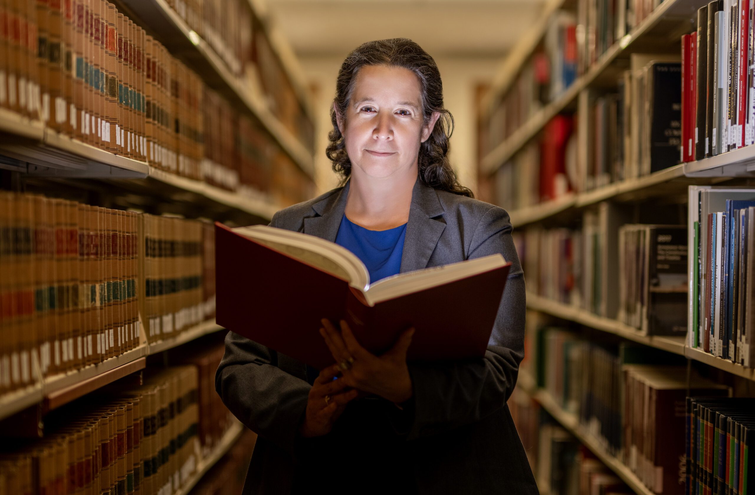 Dorit Reiss in the UC Law SF library. She looks into the camera while holding a text book with a light illuminating her face