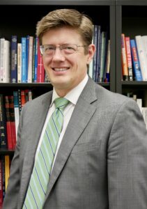 Headshot of Keith Hand in a gray suit jacket and striped green tie.