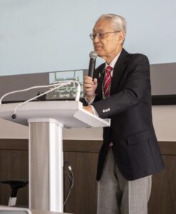 Setsuo Miyazawa holds a microphone in front of a lectern.