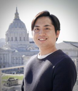 Noriyuki Issha wearing a blue sweater with the San Francisco City Hall dome in the background.