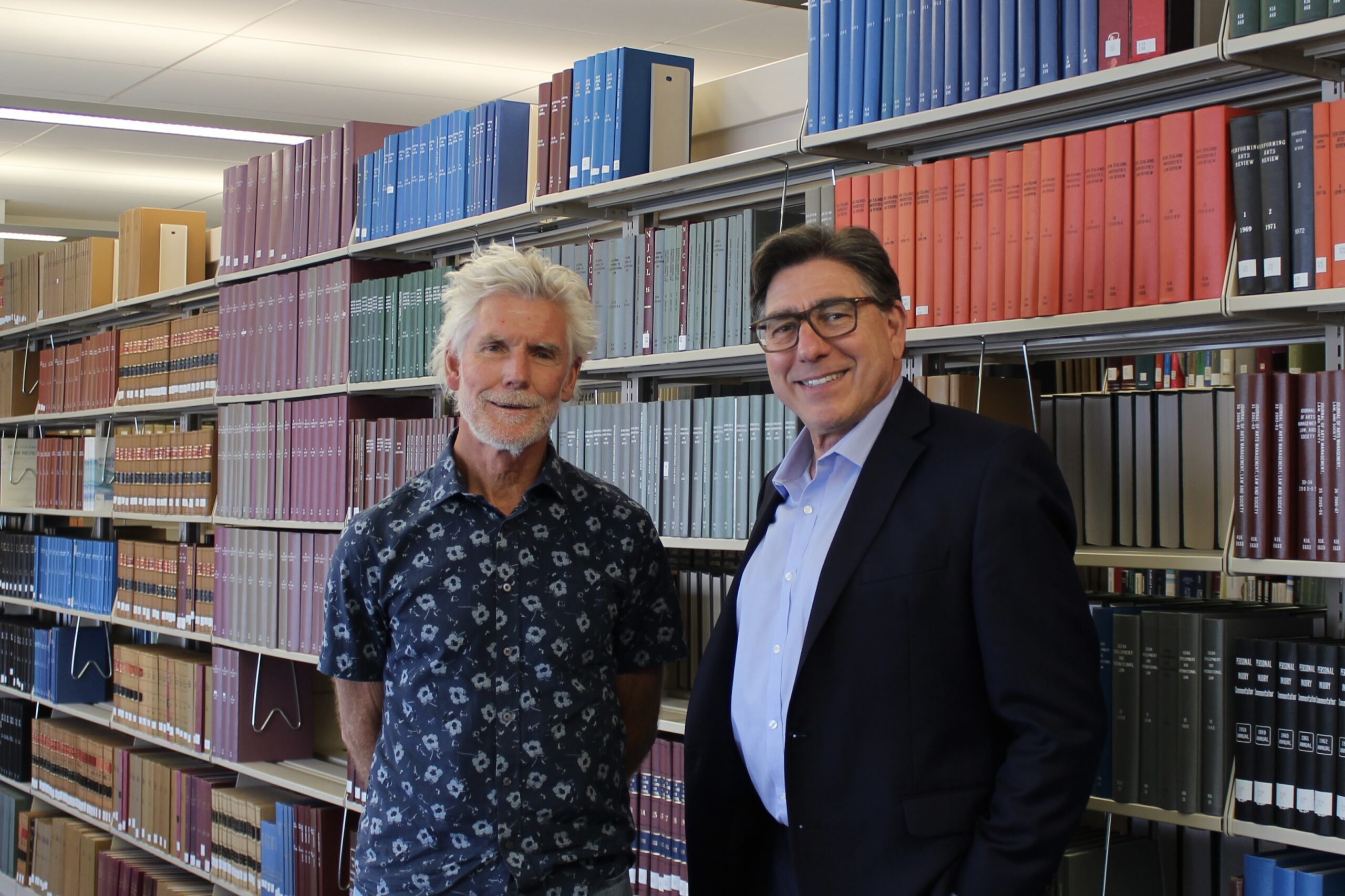 Richard Trachok poses next to David Faigman in front of a set of bookshelves in the UC Law SF library.