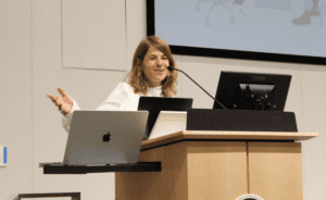 Professor Tal Niv speaking from a lectern outfitted with monitors and a microphone. 