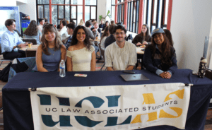 Four students from UC Law Associated Students sit at a table with a large UCLAS banner