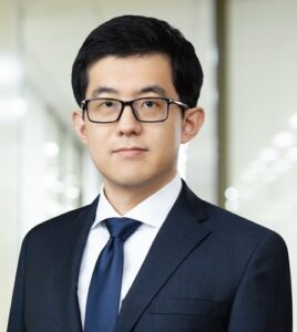 Photo of Daigo Takahashi in a navy blue suit with a blue tie and eyeglasses.