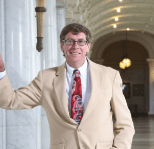 Professor Rory Little wearing a red tie and cream-colored suit.