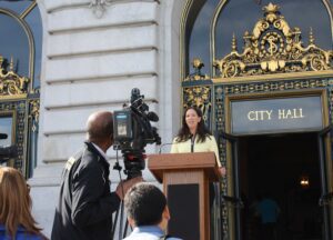 Nicole Ozer speaks at a podium in front of San Francisco City Hall.