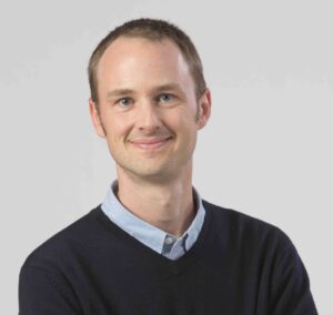 A headshot of Abraham Cable donning a dark blue professorial sweater