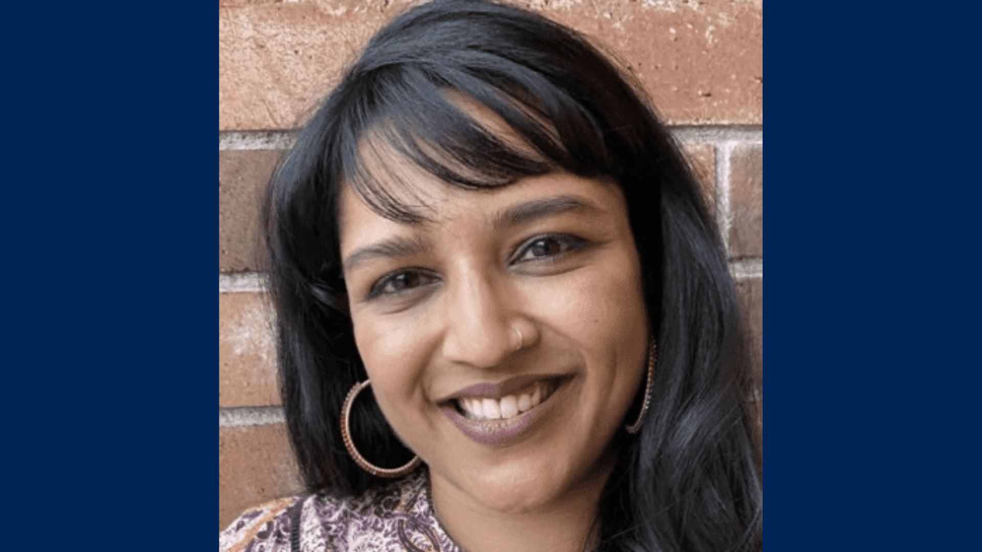A close-up photo of Seema N. Patel's face smiling with long dark hair and hoop earrings