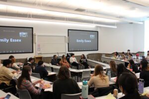 A panel with four people sits in front of a classroom full of students