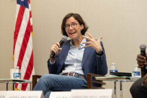 Judge Ana Reyes, seated in blue jeans with a blue blazer, speaks into a microphone.