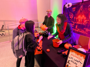 Two UCLAS representatives dressed up in Halloween costumes hand out candy to a child in the 198 McAllister auditorium