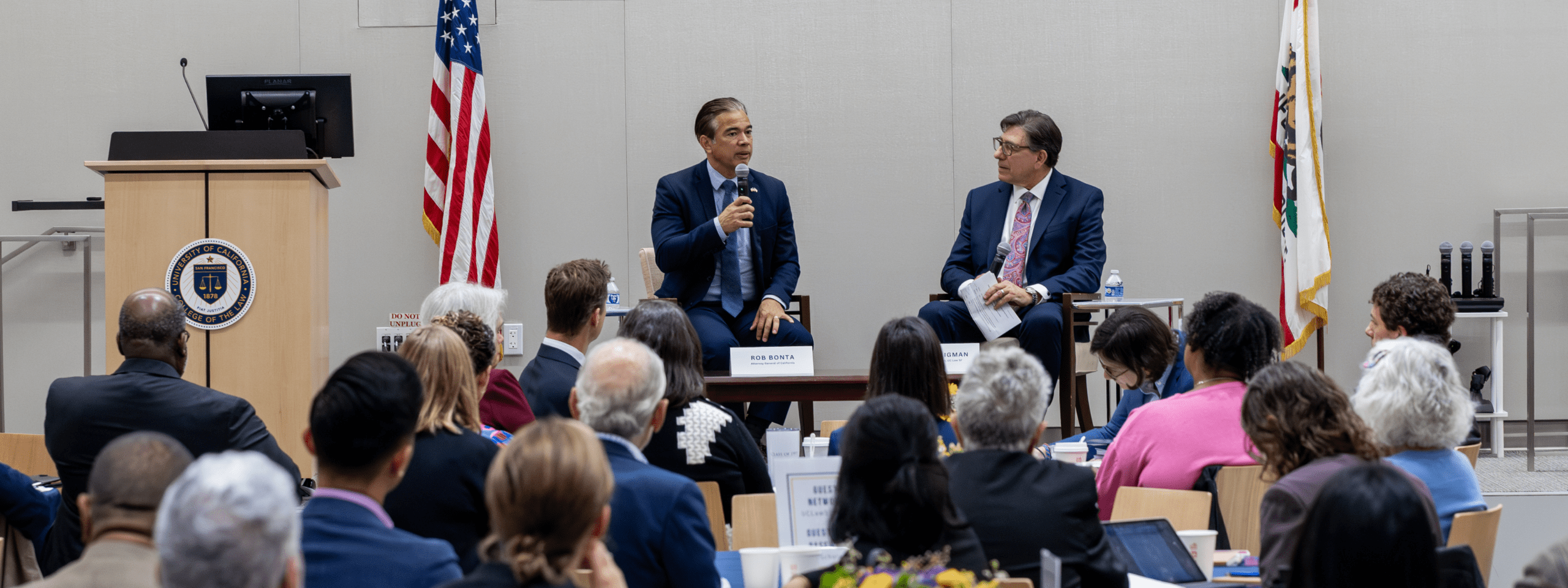 Seated next to David Faigman, Rob Bonta speaks into a microphone before a crowd of attendees in an auditorium.