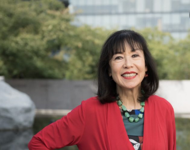Karen Korematsu, with dark hair, poses outdoors in a red dress.