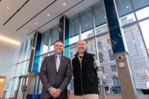 Dan Goods and Christopher Gabriel stand in the lobby of the 198 McAllister building, a digital art installation behind them.