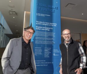 David Faigman and Dan Goods pose in front of a pillar with a blue plaque with information about the art piece.