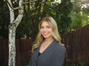3L student Katrina Simons wearing a blazer in front of a fence and a tree.