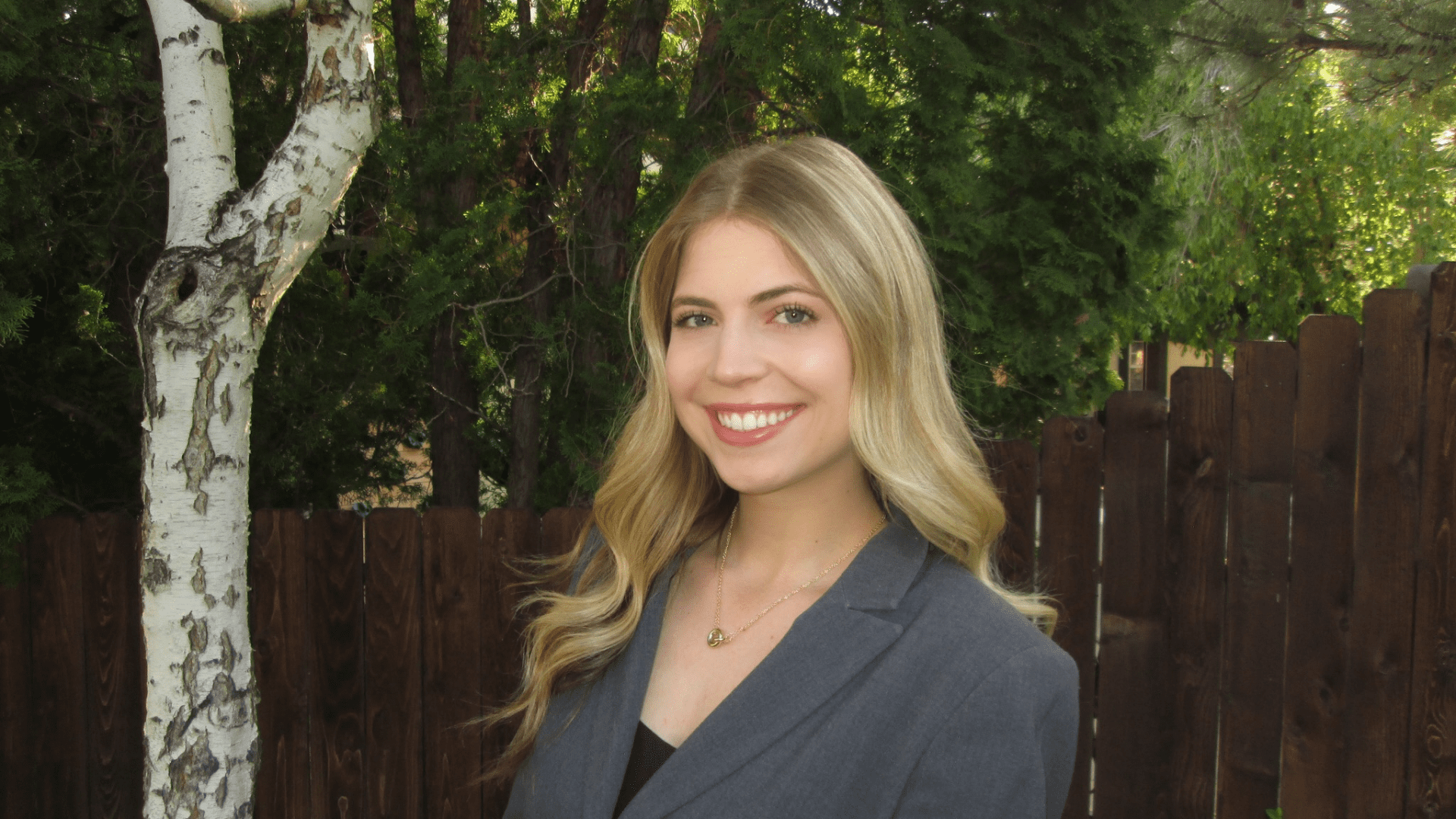 3L student Katrina Simons wearing a blazer in front of a fence and a tree.