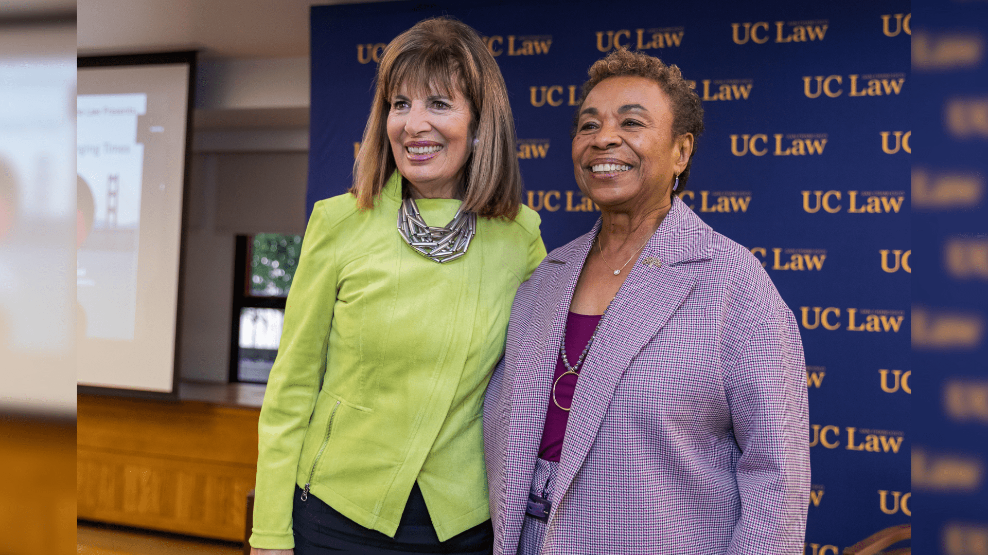 Jackie Speier and Barbara Lee smiling and standing in front of a UC Law SF backdrop at an event.