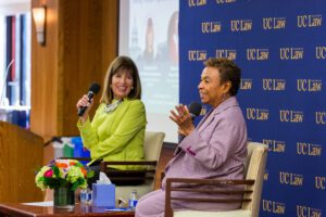 Jackie Speier ’76 and Barbara Lee holding microphones in front of a UC Law SF backdrop at an event.