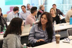 Program participants sitting behind tables talk to each other in a classroom.