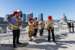 Jazz musicians play on the UC Law SF Sky Deck. They're wearing gold vests and red hats