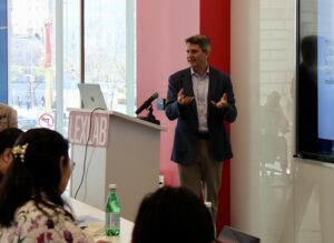 Paul Belonick speaks behind a podium at the front of a classroom.