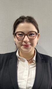 3L Nada Zohayr smiling while wearing a suit and glasses in front of a white background.