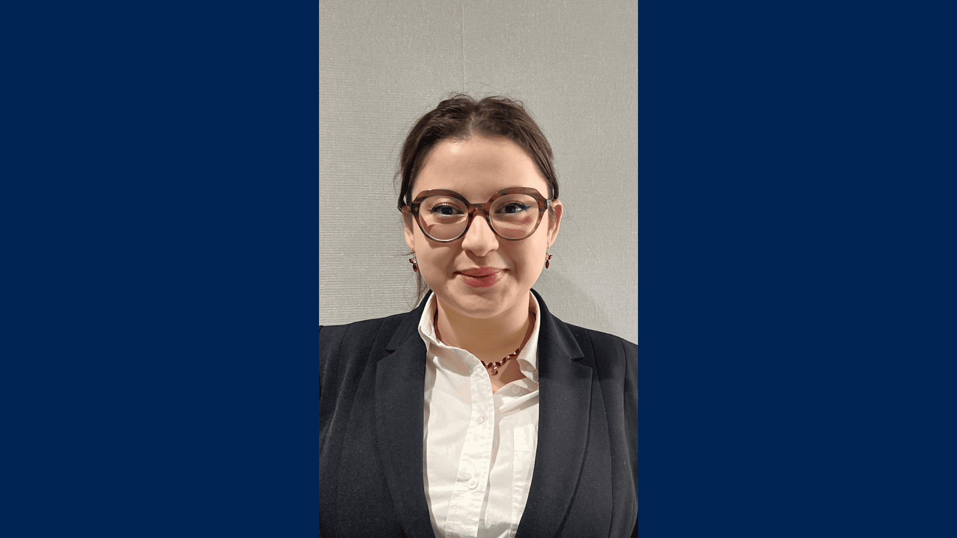 3L Nada Zohayr smiling while wearing a suit and glasses in front of a white background.