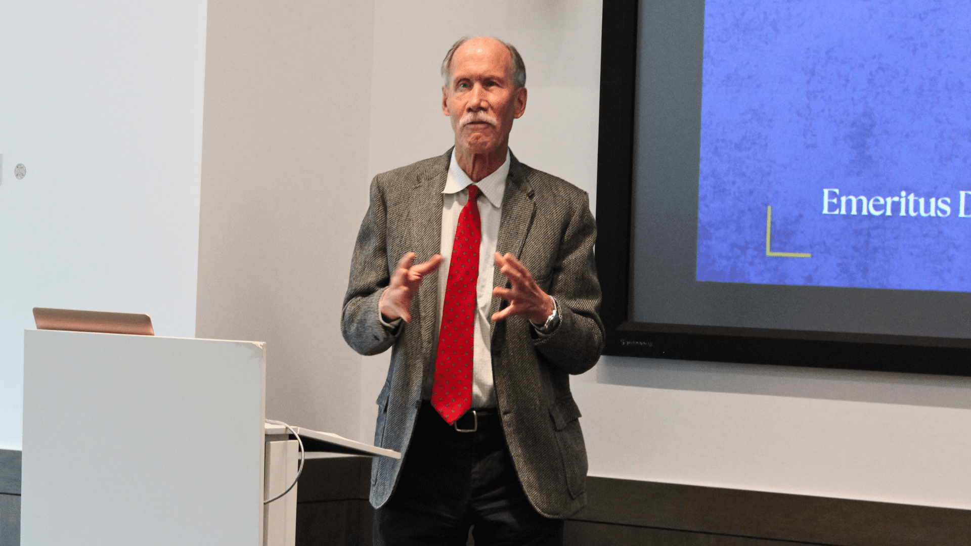 Richard Marcus speaks at the front of a classroom, gesticulating with his hands.