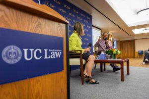Jackie Speier and Barbara Lee speak on stage next to a UC Law-branded podium.
