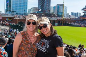 Two UC Law SF alumna smile wearing UC Law SF hats at Oracle Park