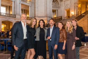 Seven UC Law SF alumni stand together and smile at the camera inside San Francisco City Hall