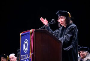 Karen Korematsu, in a black cap and gown, speaks at a podium.