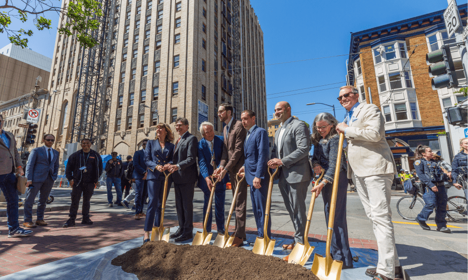 A group of people with golden shovels in front of the 100 McAllister St. Tower for the building's groundbreaking ceremony