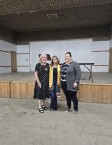 Three people posing for a photo. The student in the middle wears a graduation stole