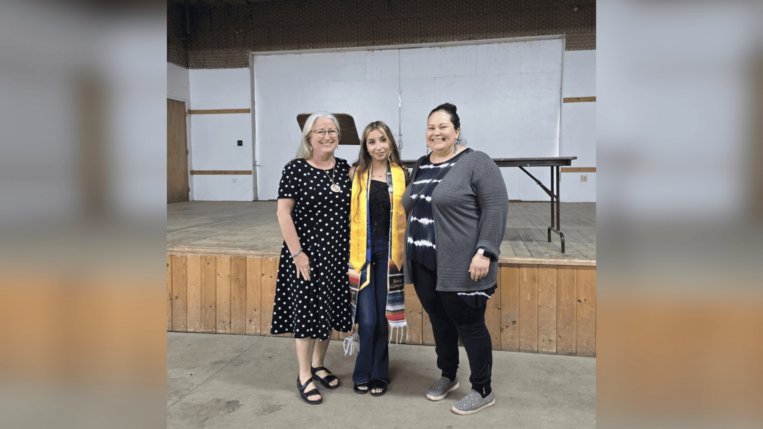 Three people posing for a photo. The student in the middle wears a graduation stole