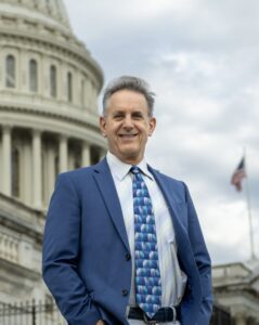Brad Kane poses in a blue suit and tie in front of the U.S. Capitol building.