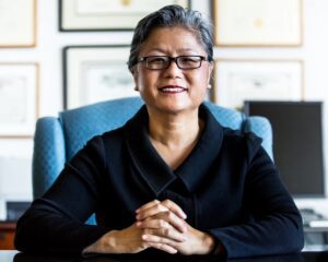 Susan Chung sits behind a desk wearing a black suit and eyeglasses.