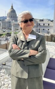 Susan Chung poses on the Sky Deck of UC Law SF's Cotchett Law Center in an olive-colored business suit and black sunglasses with folded arms.