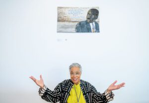 Alice Beasley poses while standing beneath her artwork affixed to the wall.