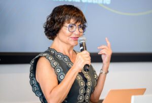 Esther Mallouh speaks while holding a microphone.