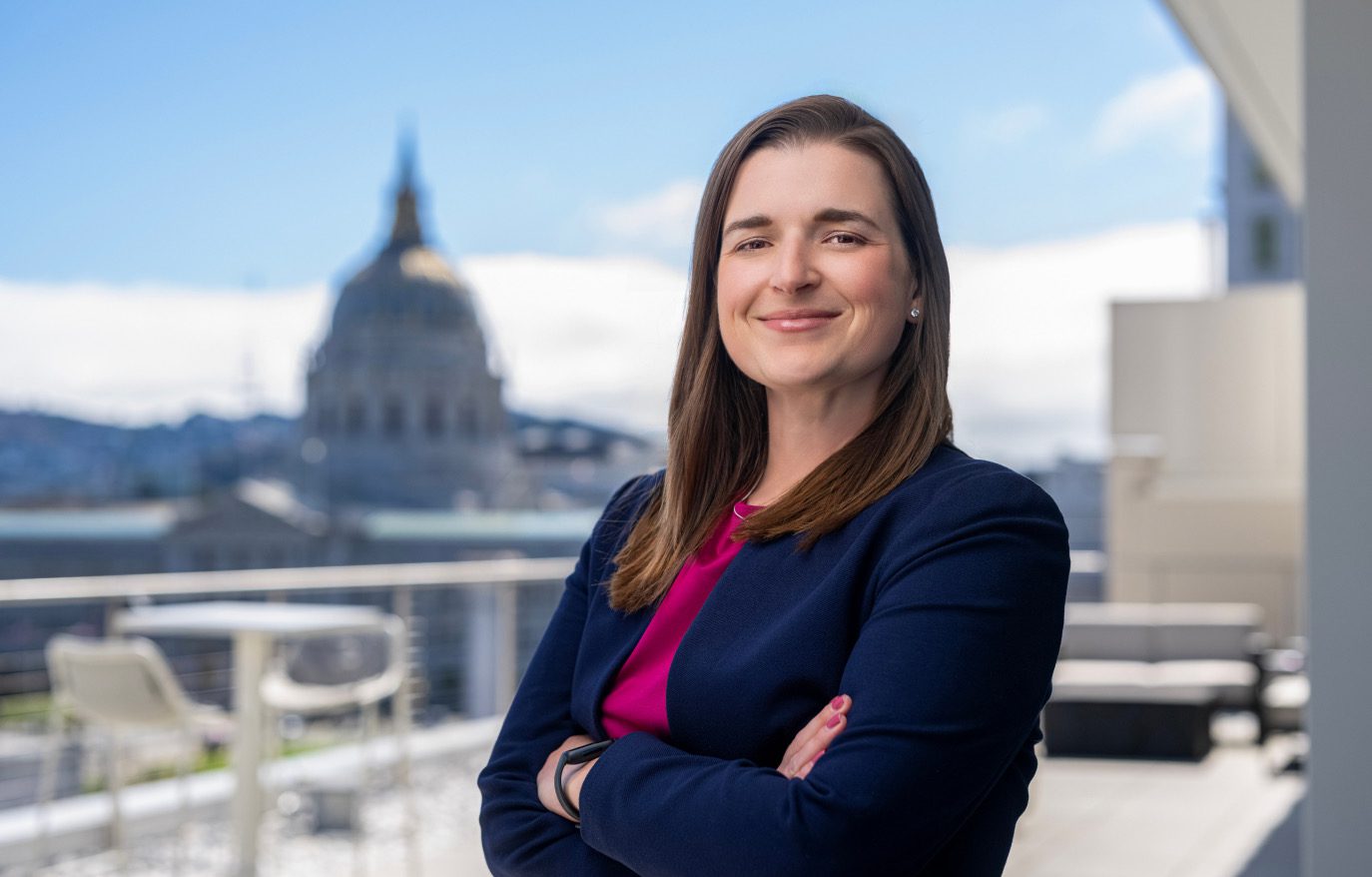 An alumna on a rooftop with San Francisco City Hall behind her