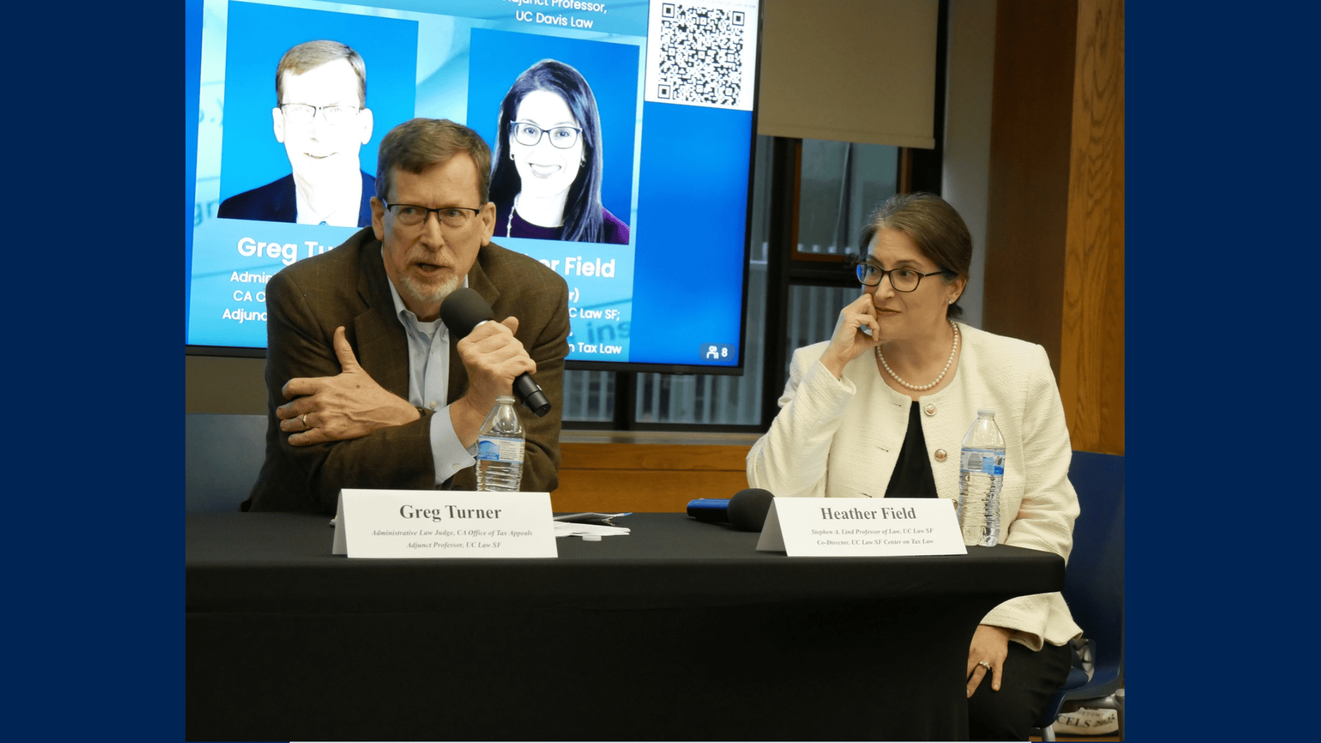 Greg Turner speaks into a microphone as Heather Field sits beside him attentively.
